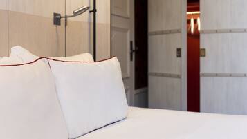 A hotel room with a bed, pillows, and a door leading to another room.
