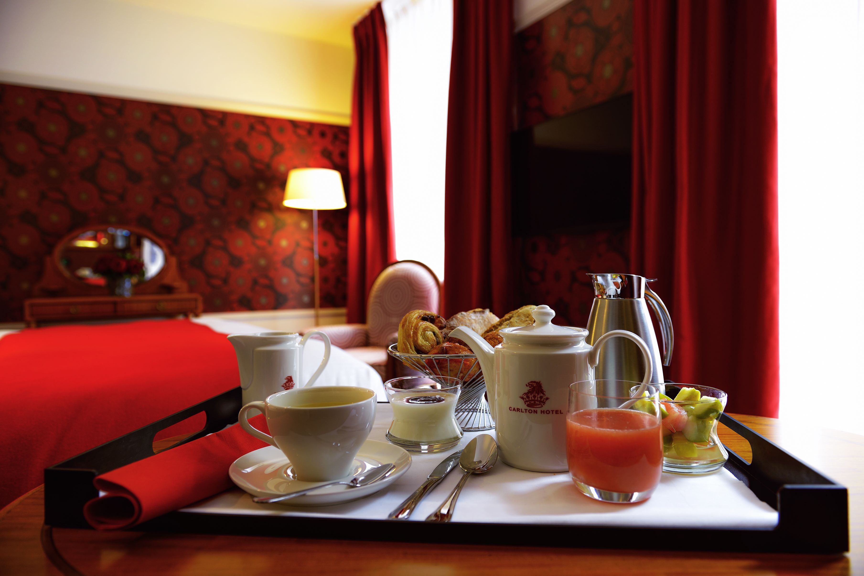 A breakfast tray with a cup, saucer, spoon, knife, jug, and a glass of juice.