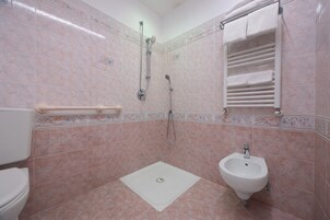 A bathroom with pink tiles, a shower, a bidet, and a towel rack.