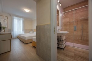 A modern hotel room with a large bed, a separate bathroom with a glass shower, and a small sitting area with a table and chairs.