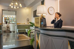 A hotel reception area with a reception desk, a clock, a bar, and seating. - Hotel Palladium Palace (Rome)
