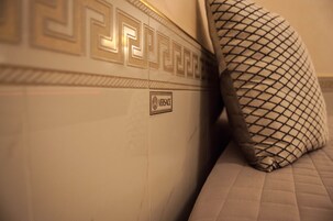 A bed with a patterned pillow and a wall with a decorative design and a 'Versace' logo.