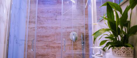 A modern bathroom with a glass-enclosed shower, a wooden wall, and a potted plant.