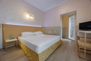 Una camera d'albergo moderna con un letto grande, un comodino e una TV su una scrivania.