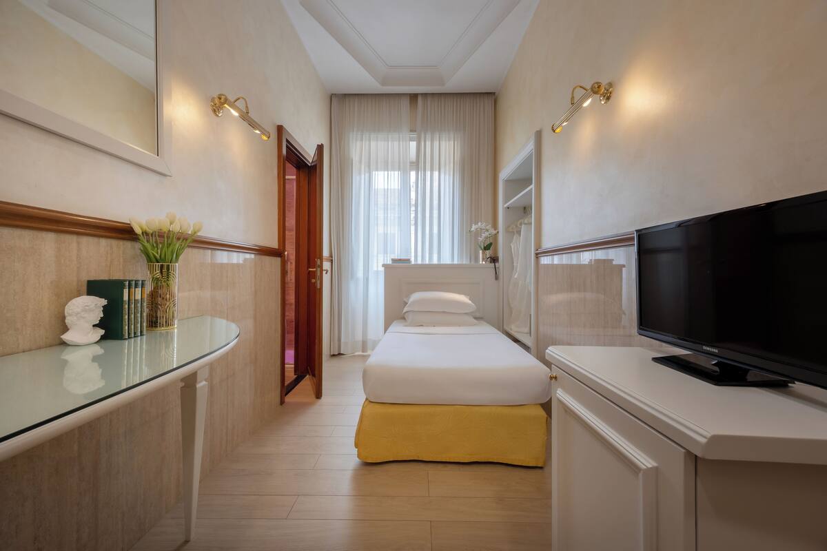 Ein Hotelzimmer mit Bett, Fernseher, Schreibtisch und einer Blumenvase sowie einem Spiegel.
