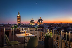 Una terraza con una mesa, sillas y vistas a edificios históricos al atardecer.