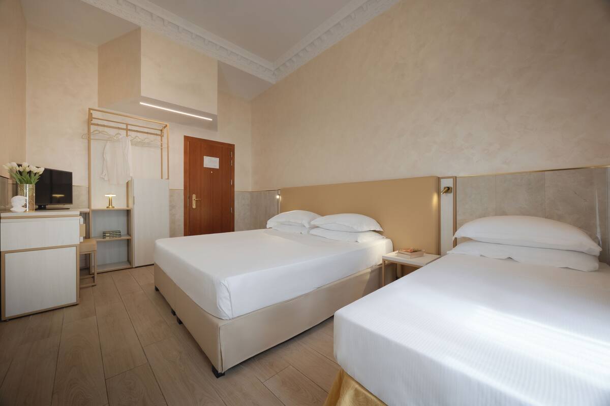 Ein Hotelzimmer mit zwei Betten, einem Schreibtisch, einem Fernseher und einem Kleiderschrank.