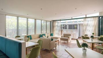 A modern hotel lobby with seating areas, tables, and large windows.