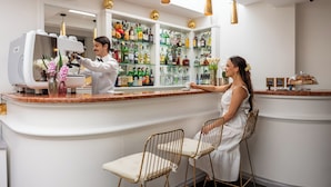 A bar area with a counter, shelves of bottles, and two chairs. - Hotel Palladium Palace (Rome)