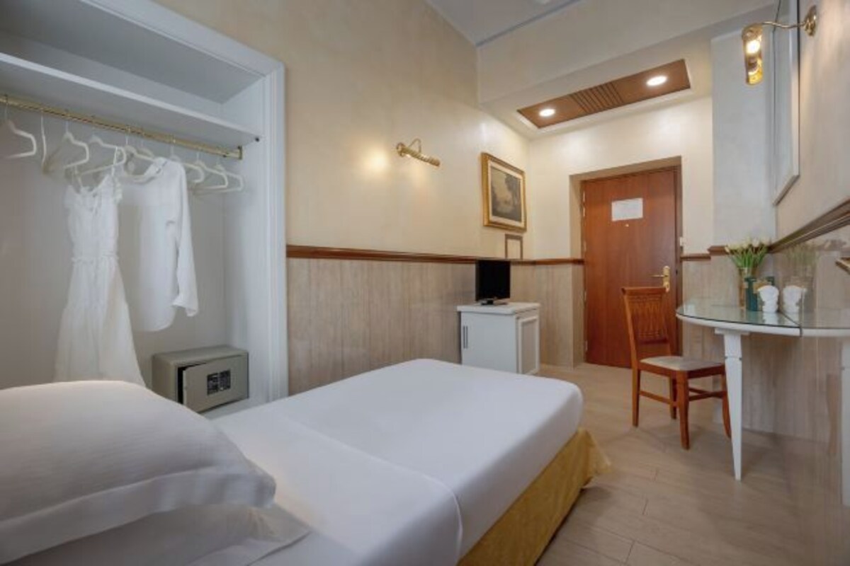 Una habitación de hotel con cama, escritorio, silla y un pequeño armario.