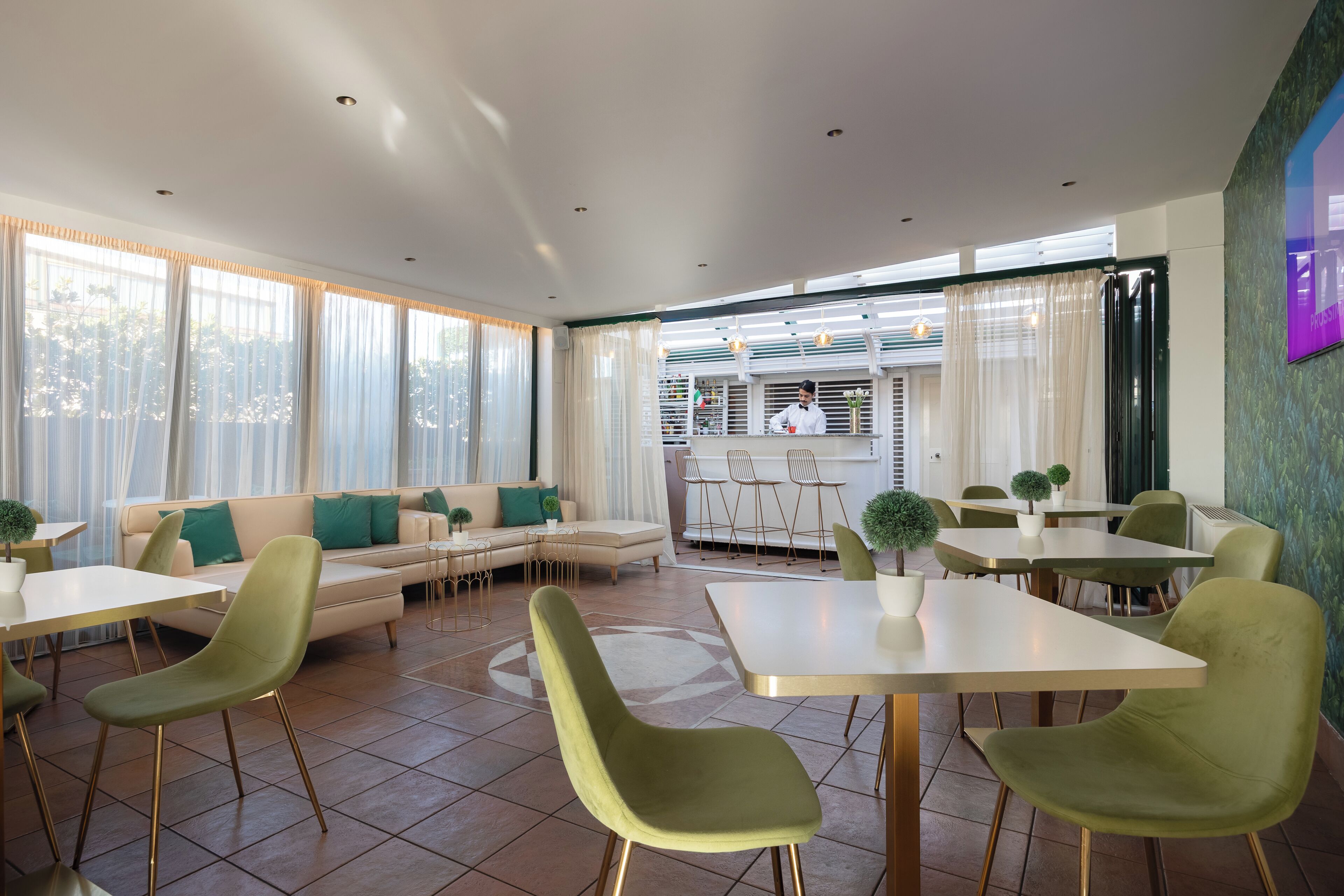 A modern dining area with green chairs, white tables, and a sofa with green cushions.