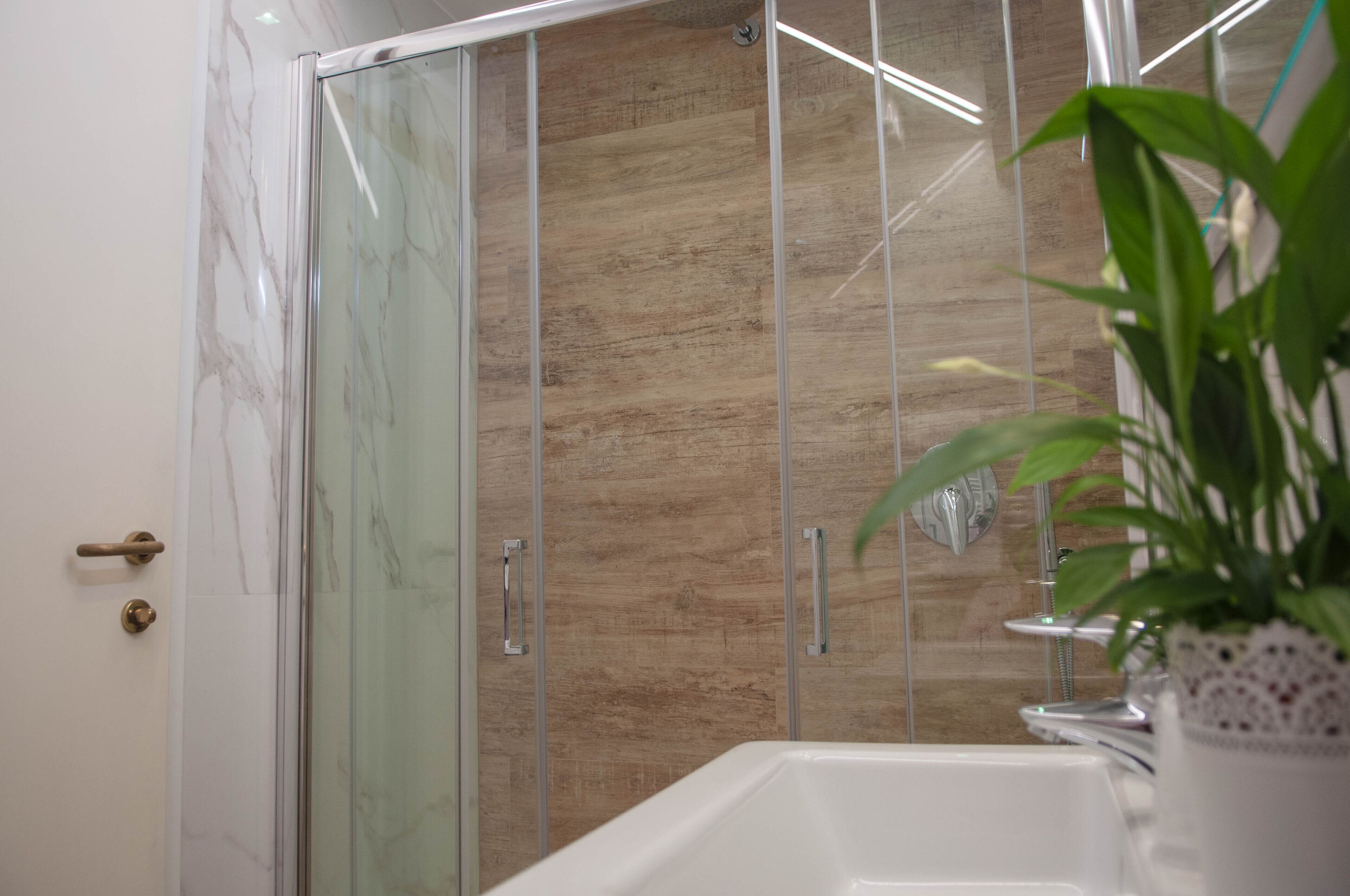 Un baño moderno con cabina de ducha de vidrio, tocador de madera y una planta en maceta.