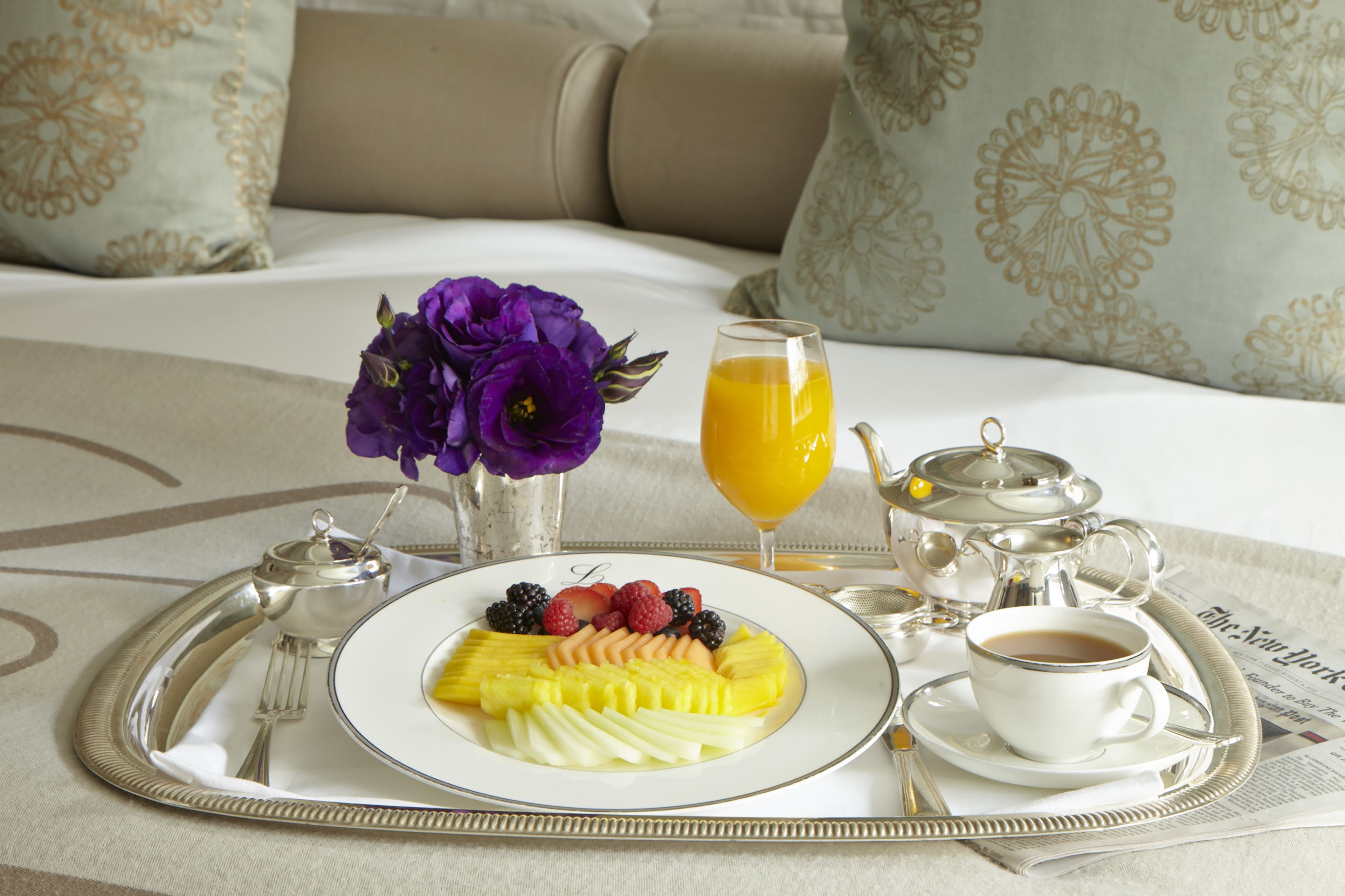 A breakfast tray with fruit, a cup of coffee, and a glass of orange juice on a bed with a floral bedspread.
