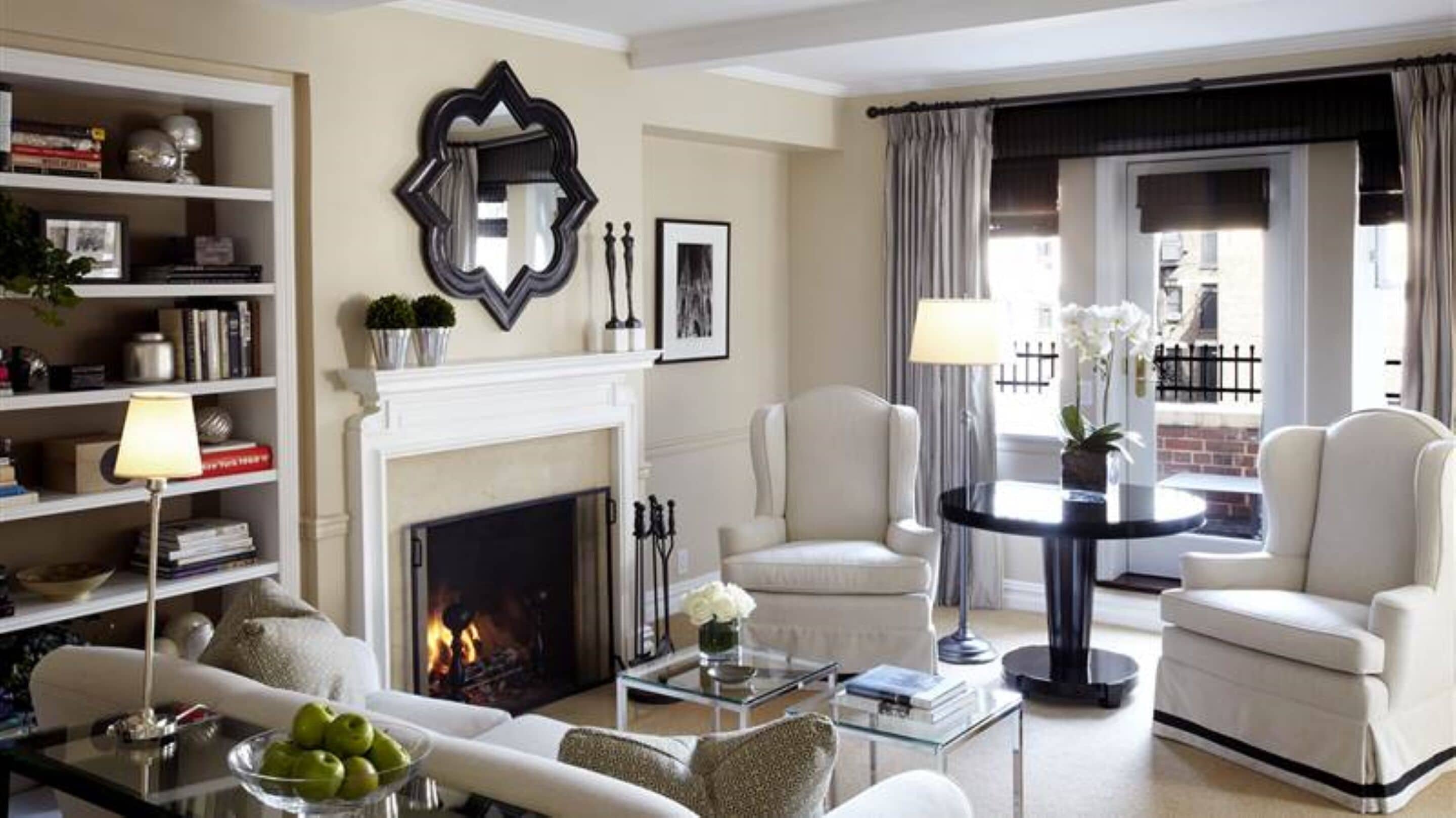 A living room with a fireplace, white armchairs, a sofa, a coffee table, and a bookshelf.
