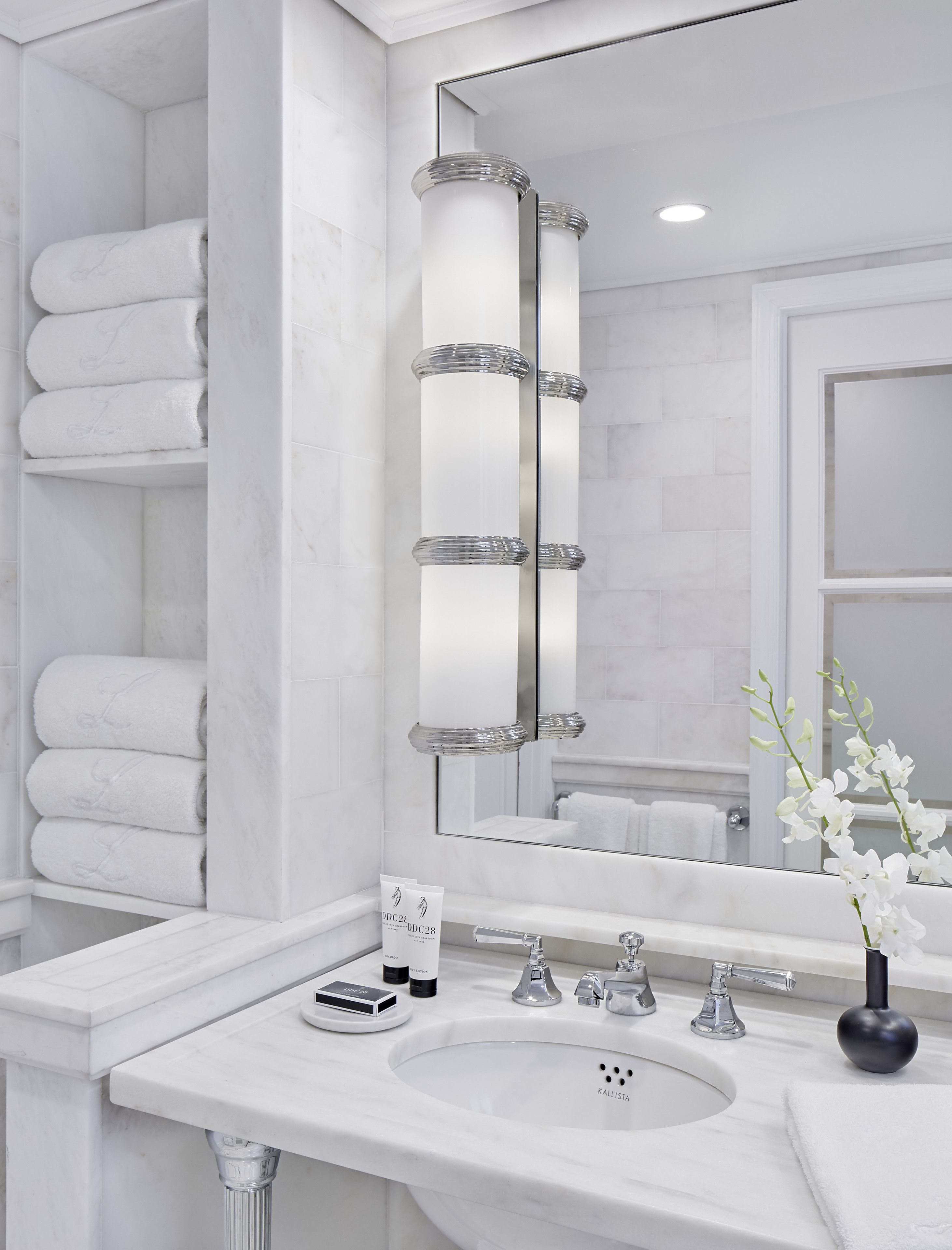 Un baño moderno con un lavabo de mármol, un espejo grande con luces y toallas ordenadas.
