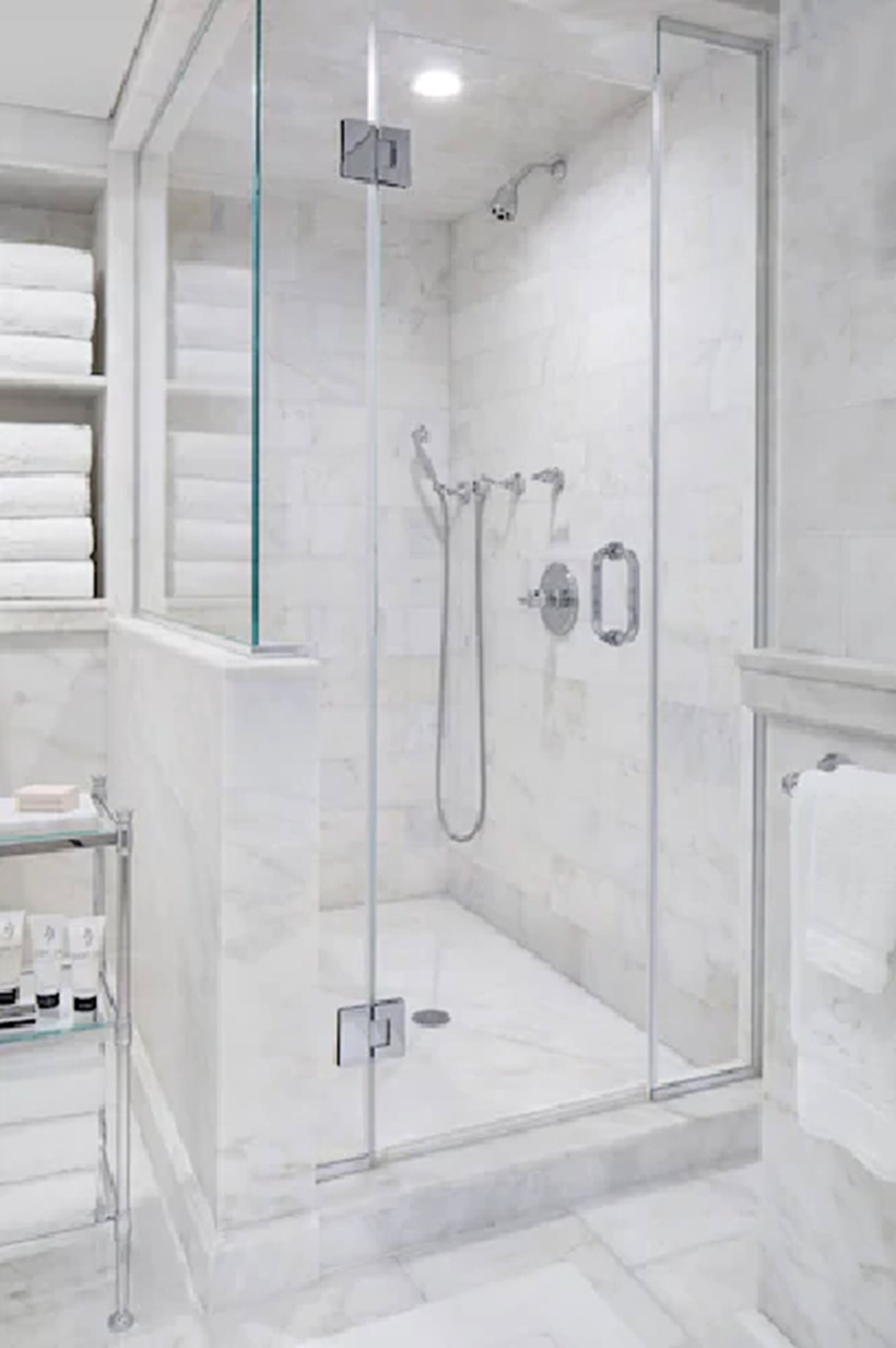A modern bathroom with a glass-enclosed shower, marble walls, and neatly arranged towels.