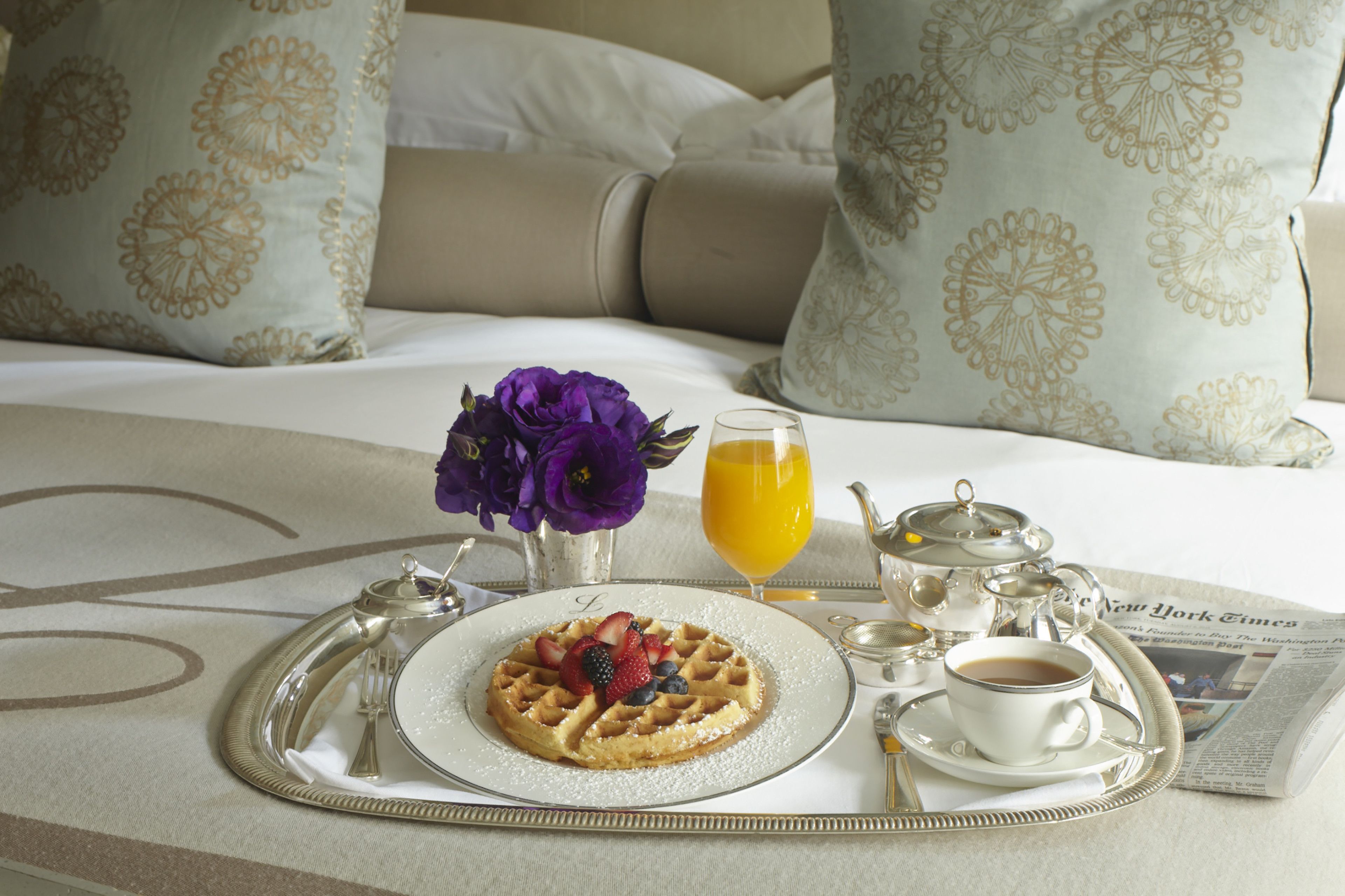 Ein Frühstücksbrett mit Waffeln, Kaffee und Saft auf einem Bett mit blumigen Kissen.