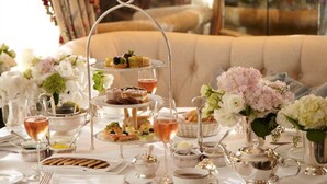 A three-tiered dessert stand with pastries and a glass of rosé wine on a table with white tablecloths and silverware. - The Lowell (New York)