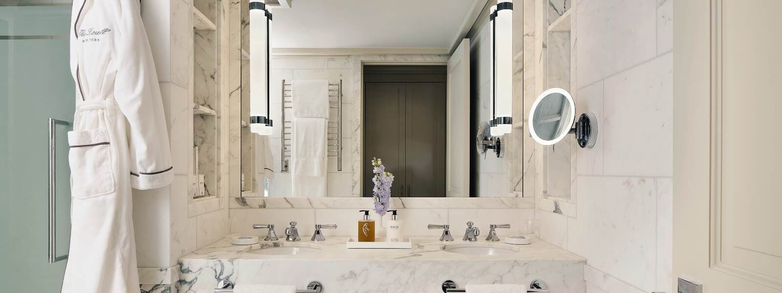 Een moderne badkamer met twee wastafels, een grote spiegel en een badjas hangend aan de muur.