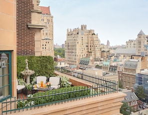 A rooftop terrace with a view of surrounding buildings, a small table with chairs, and a decorative fountain.