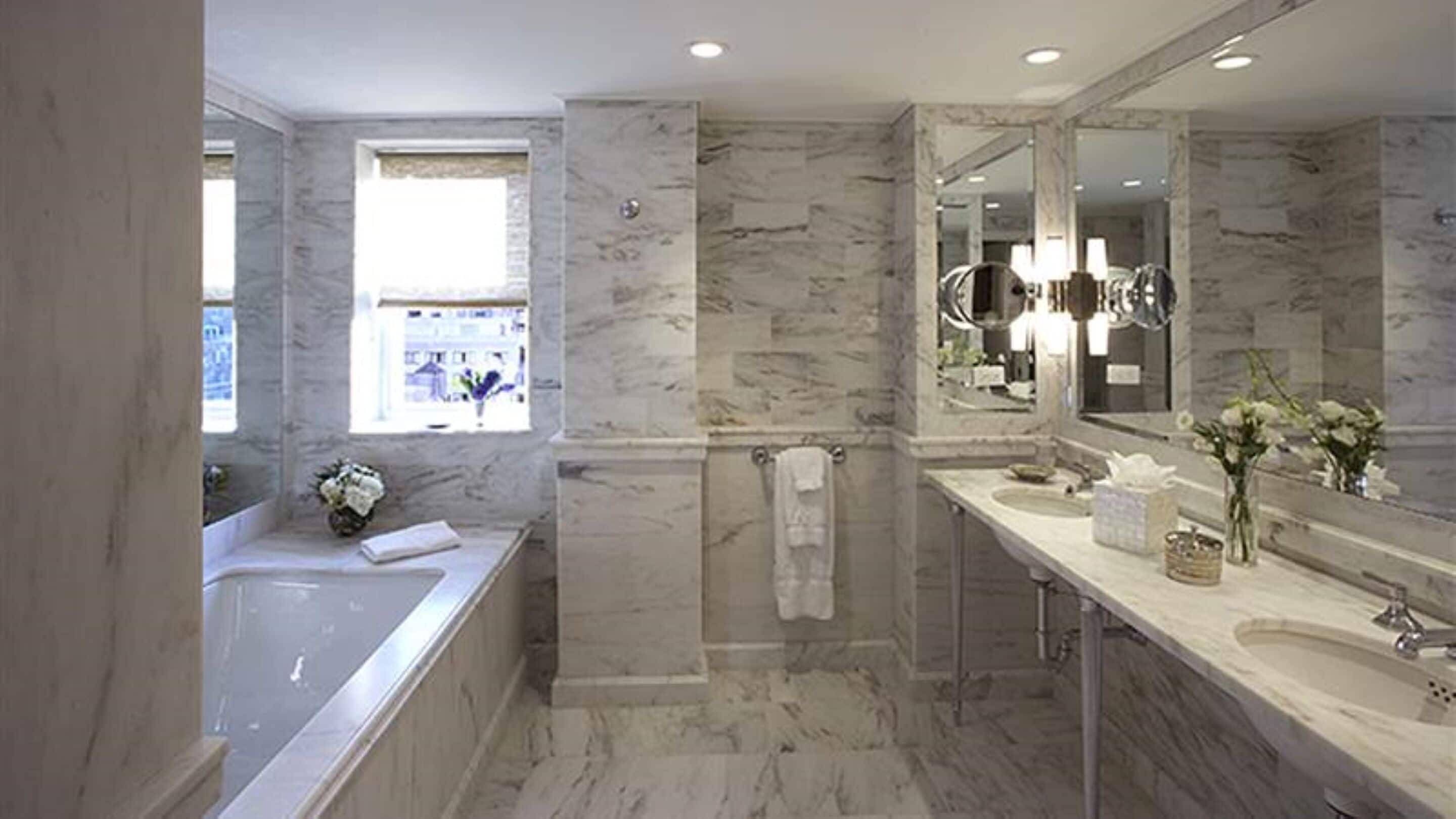 Une salle de bain moderne avec un sol en marbre, une grande baignoire, un meuble-lavabo à deux vasques et un grand miroir.