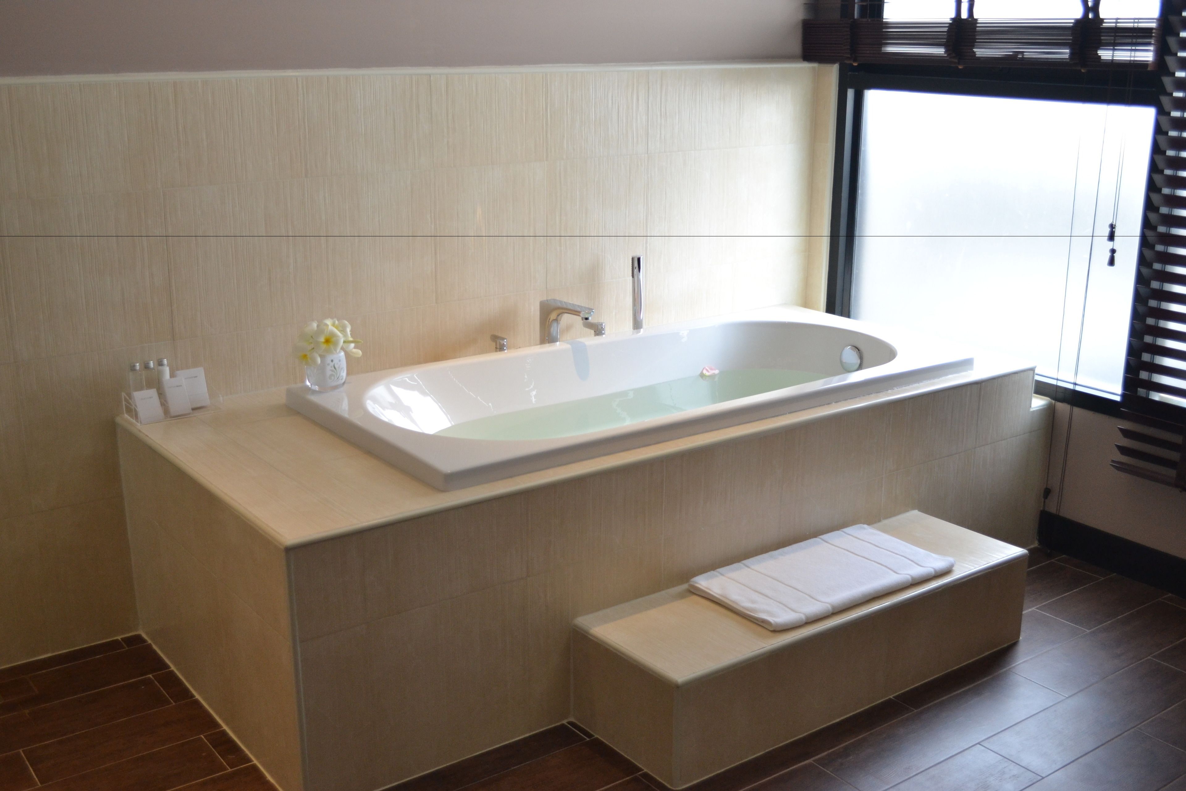 A modern bathroom with a freestanding bathtub, a bench, and a window providing natural light.