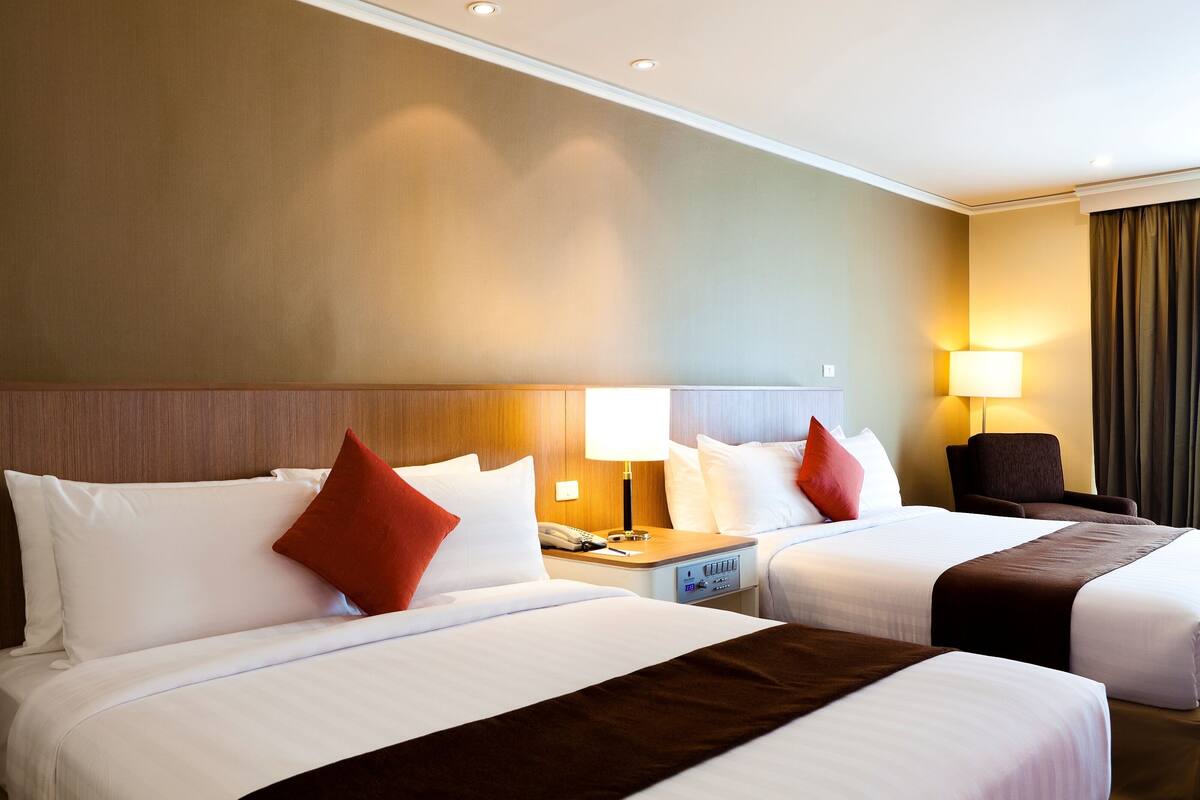 A hotel room with two beds, a nightstand with a phone, and a lamp.
