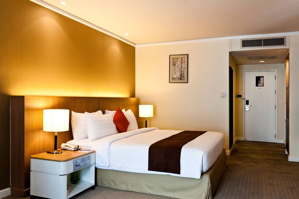 A hotel room with a large bed, two bedside lamps, a nightstand with a phone, and a door leading to another room.