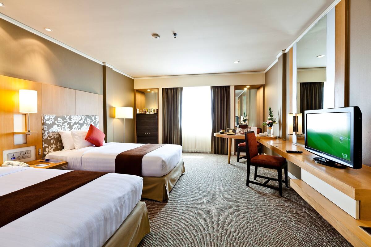 A hotel room with two beds, a desk with a TV, a chair, and a bathroom visible through a door.