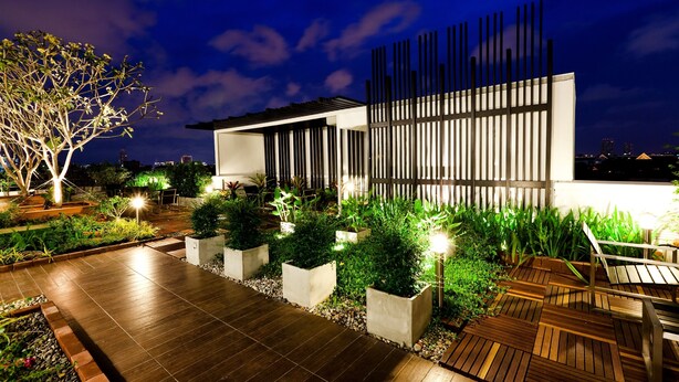 Un patio moderno al aire libre con terraza de madera, macetas de hormigón y diversas plantas.