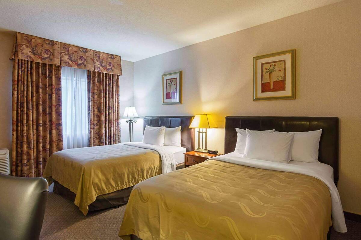 A hotel room with two beds, a desk, a chair, and two lamps.