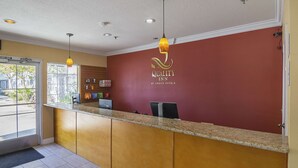 A hotel reception area with a red wall, a reception desk, and a glass door leading outside. - Quality Inn Fresno Yosemite Airport (Fresno)