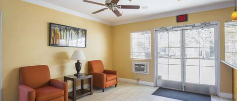 Une pièce avec deux fauteuils orange, un ventilateur de plafond, un tableau et une porte avec un panneau indiquant la sortie.