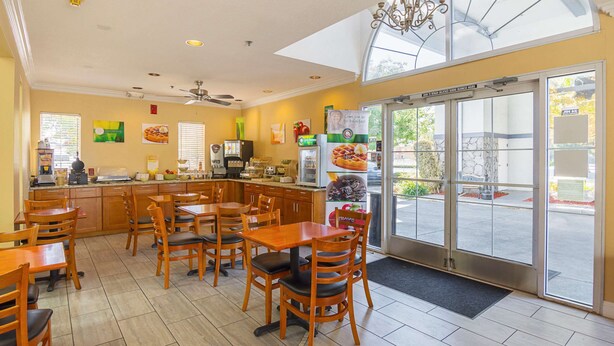 A restaurant with a kitchen area, dining tables, chairs, and a large window with a view of the street. - Quality Inn Fresno Yosemite Airport (Fresno)