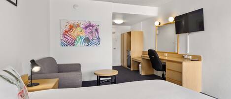Une chambre d’hôtel avec un lit, un bureau, une chaise, une petite table, un canapé, une télévision et un tableau au mur.