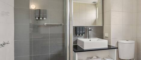Un baño moderno con cabina de ducha de vidrio, un lavabo blanco y un inodoro.