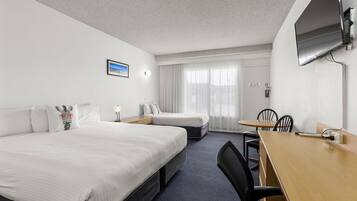 A hotel room with two beds, a desk, chairs, a TV, and a window with curtains.