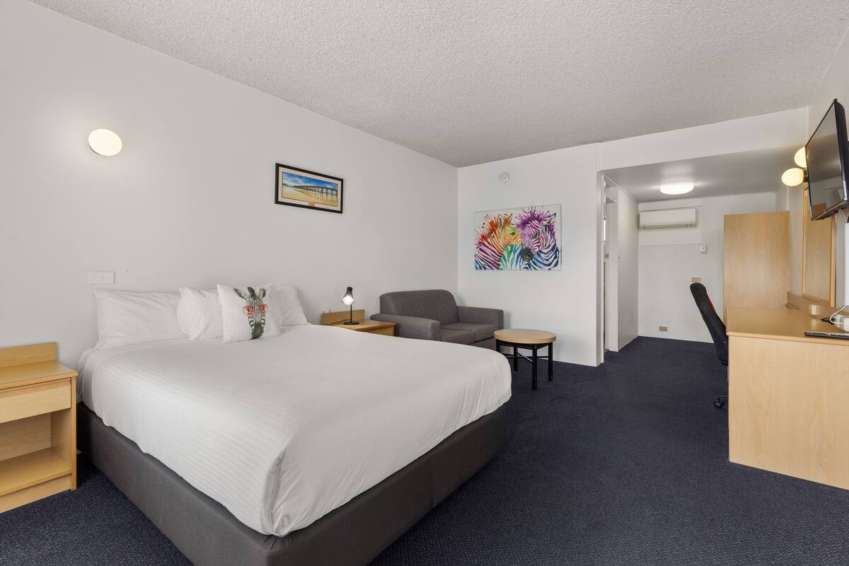 Une chambre d’hôtel avec un grand lit, un bureau, une chaise et un téléviseur.