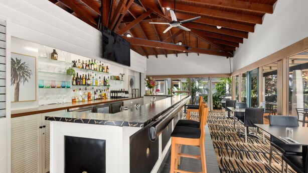 A modern bar area with a wooden ceiling, a large TV, and a variety of bottles and glasses on shelves. - Zebra Motel   (Coffs Harbour)