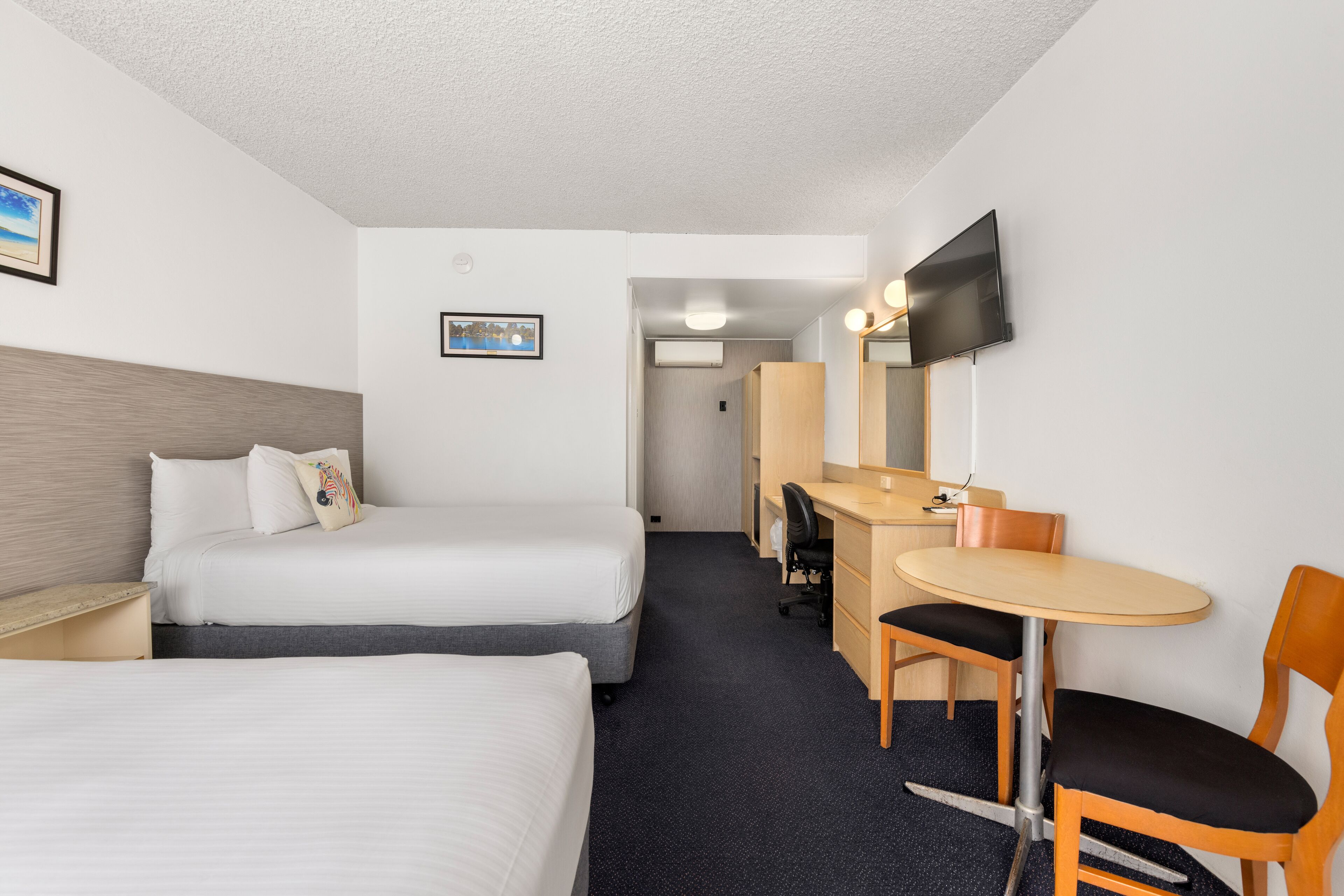 A hotel room with two beds, a desk, a chair, a TV, and a mirror.