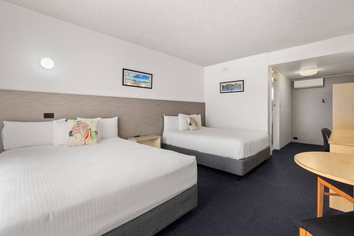 Une chambre d’hôtel avec deux lits, un bureau et une chaise. Deux tableaux encadrés sont accrochés au mur.