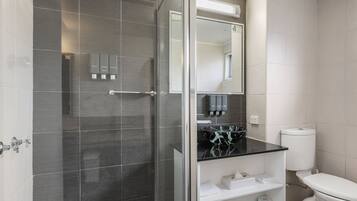 Un baño moderno con ducha de vidrio, lavabo de mármol negro y retrete blanco.