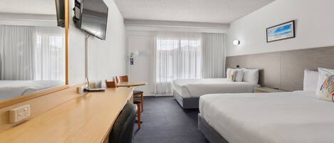 A hotel room with a large bed, a smaller bed, a desk with a chair, a TV mounted on the wall, and a window with curtains.
