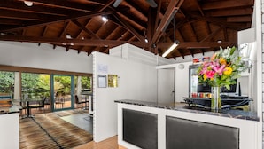 A modern kitchen with a large island, a dining area with outdoor views, and a ceiling with exposed beams. - Zebra Motel   (Coffs Harbour)