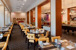 Comedor de hotel con varias mesas dispuestas para los huéspedes, una zona de bar con diversas bebidas y vistas al interior del hotel.