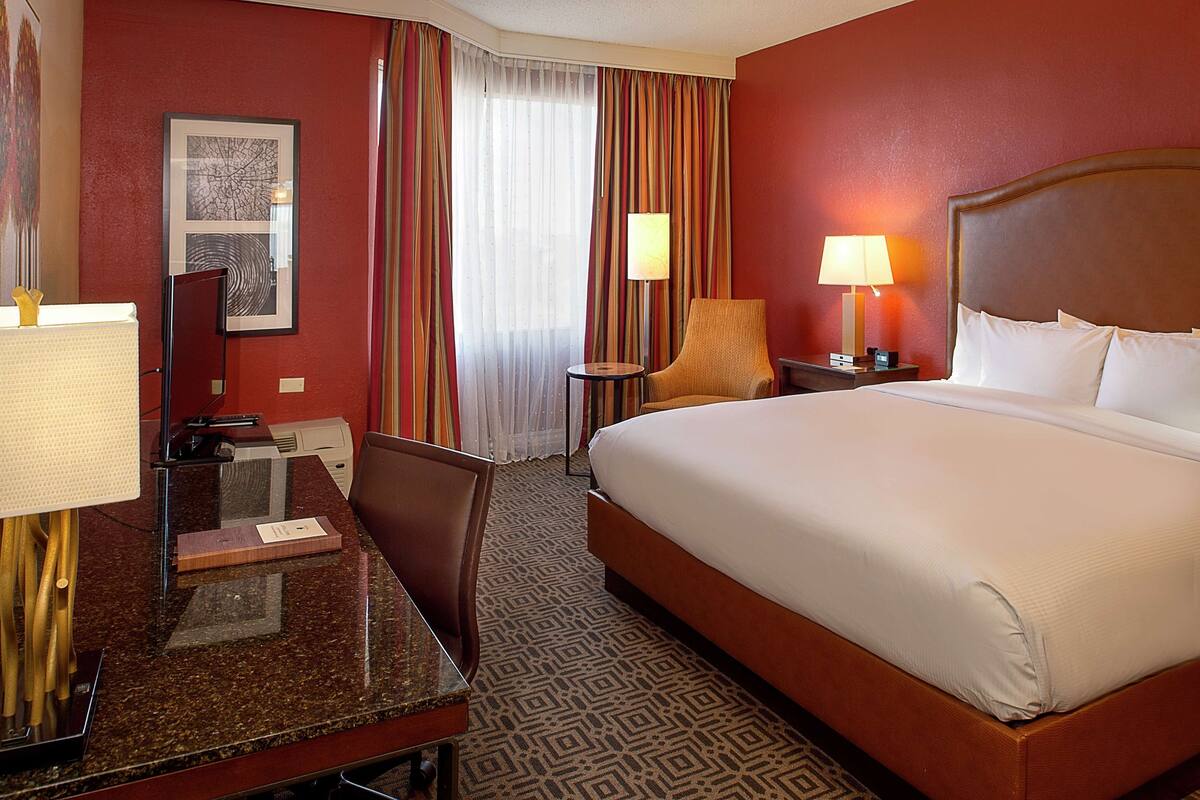 Une chambre d’hôtel avec un grand lit, un bureau avec une chaise, une petite table avec une lampe et un tableau au mur.