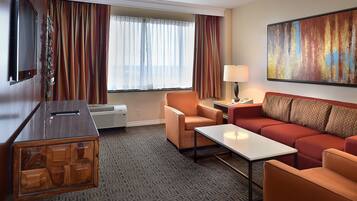 A hotel room with a sofa, armchair, coffee table, TV, and artwork on the wall.