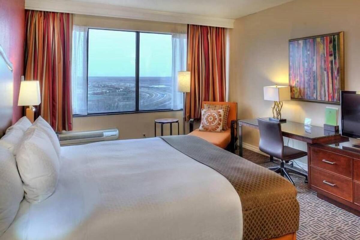 Une chambre d’hôtel avec un grand lit, un bureau, une chaise, une télévision et un tableau au mur.