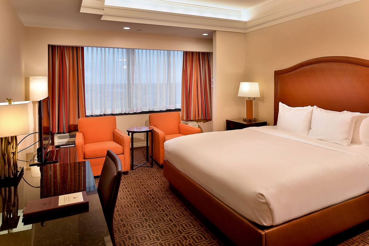 Une chambre d’hôtel avec un grand lit, un fauteuil orange, une petite table et un bureau avec une lampe.