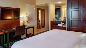 Ein Hotelzimmer mit einem großen Bett, einem Schreibtisch mit Stuhl, einem Fernseher, einem Spiegel und einem Kleiderschrank.